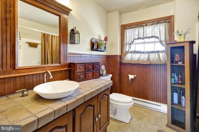 bathroom with baseboard heating, wooden walls, vanity, and toilet