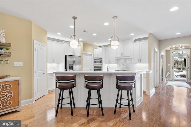 kitchen with tasteful backsplash, white cabinetry, appliances with stainless steel finishes, and decorative light fixtures