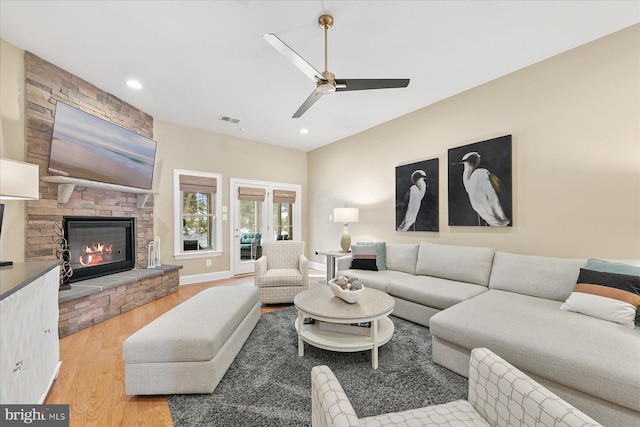 living room featuring a stone fireplace, ceiling fan, and light hardwood / wood-style flooring