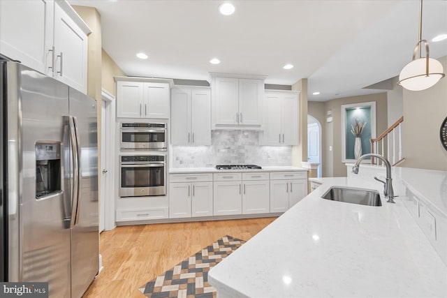 kitchen featuring sink, hanging light fixtures, appliances with stainless steel finishes, light stone countertops, and white cabinets