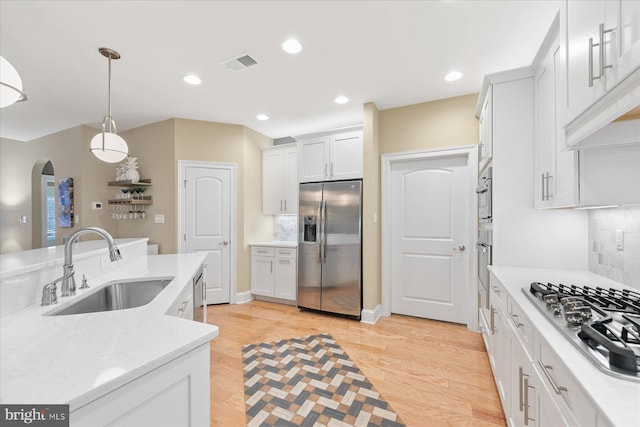 kitchen featuring sink, light hardwood / wood-style flooring, stainless steel appliances, white cabinets, and decorative light fixtures