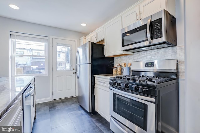 kitchen featuring appliances with stainless steel finishes, white cabinetry, decorative backsplash, dark tile patterned floors, and light stone counters