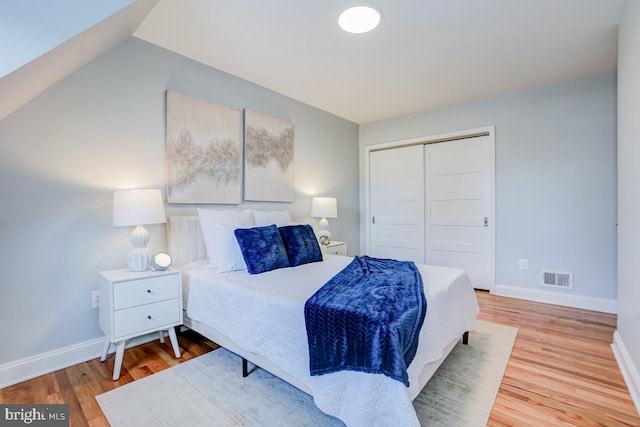 bedroom with wood-type flooring, vaulted ceiling, and a closet