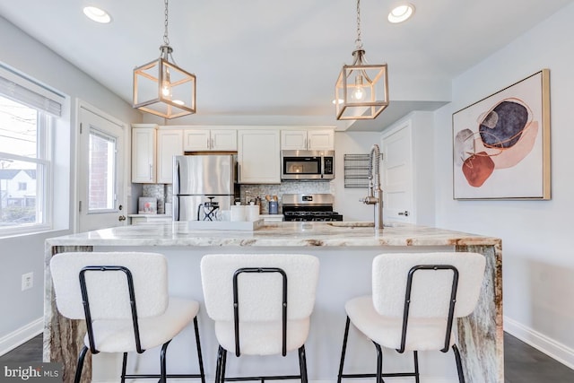 kitchen featuring tasteful backsplash, pendant lighting, stainless steel appliances, a kitchen island with sink, and white cabinets