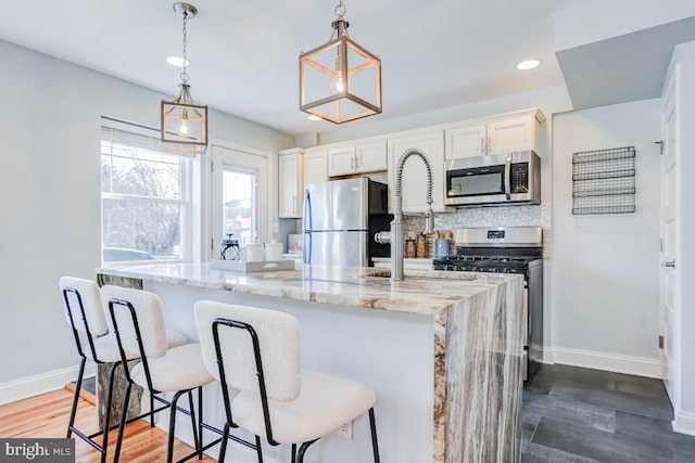 kitchen with decorative light fixtures, white cabinets, light stone counters, stainless steel appliances, and a center island with sink