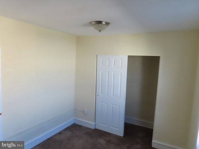 unfurnished bedroom with dark carpet and a closet