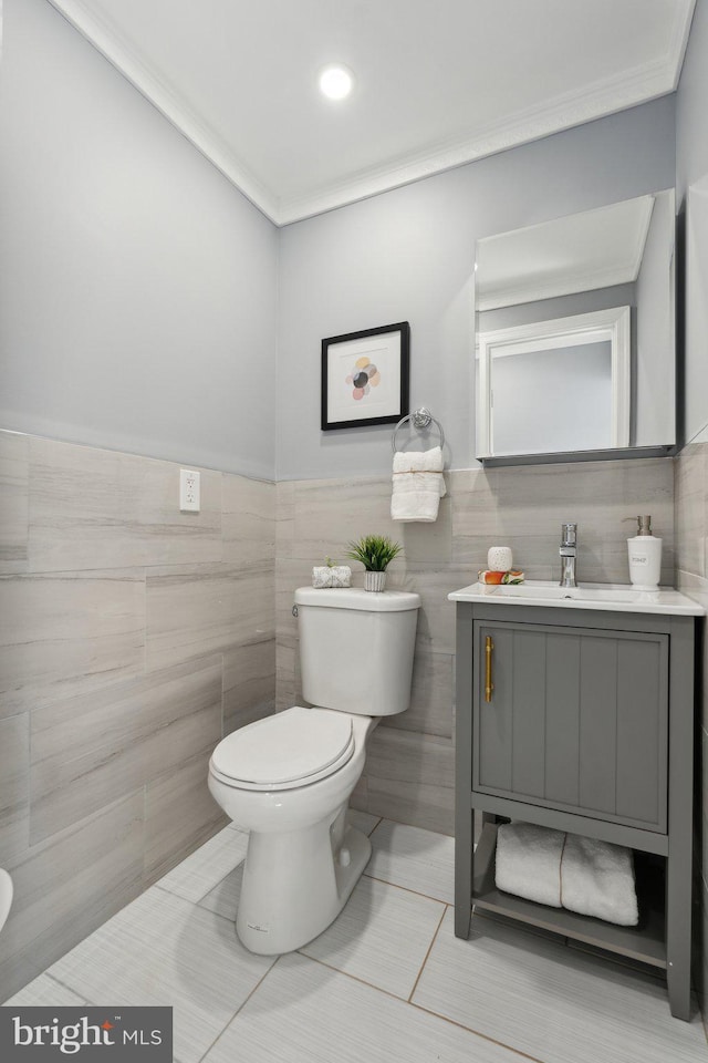 bathroom with tile patterned floors, vanity, crown molding, tile walls, and toilet