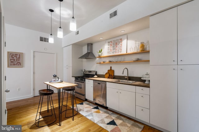 kitchen featuring wall chimney exhaust hood, stainless steel appliances, sink, white cabinetry, and hanging light fixtures