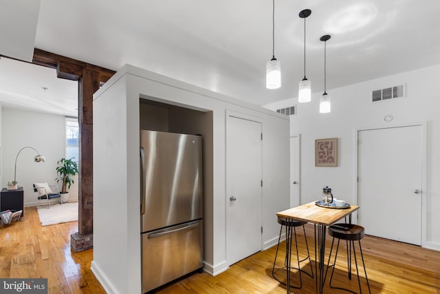 kitchen featuring stainless steel fridge, light hardwood / wood-style flooring, and hanging light fixtures