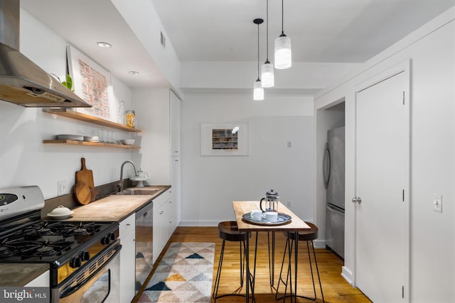 kitchen featuring stainless steel appliances, wall chimney range hood, sink, decorative light fixtures, and light hardwood / wood-style flooring