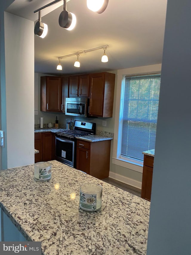 kitchen with hardwood / wood-style floors, stainless steel appliances, light stone counters, and hanging light fixtures