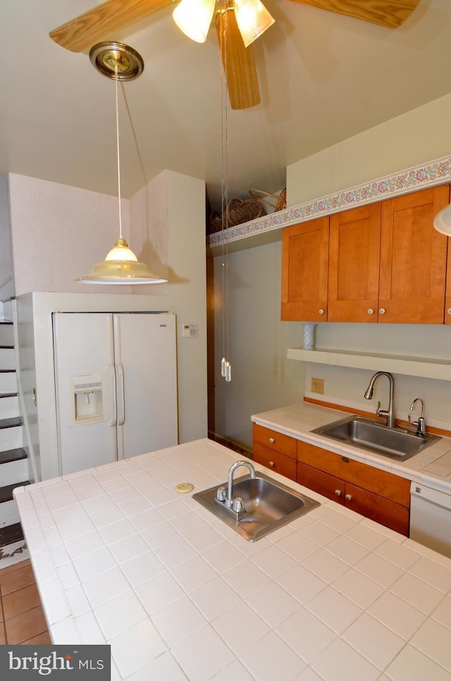 kitchen featuring sink, white appliances, hanging light fixtures, and tile counters