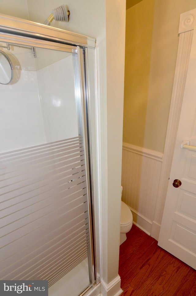 bathroom with toilet, a shower with door, and wood-type flooring