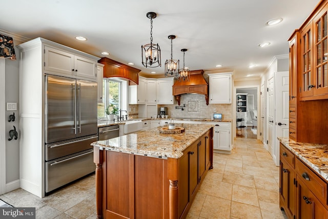 kitchen with white cabinetry, custom range hood, built in refrigerator, a kitchen island, and decorative light fixtures