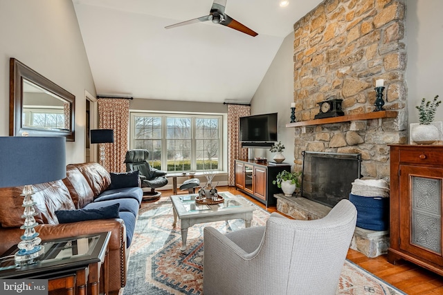 living room featuring vaulted ceiling, ceiling fan, light hardwood / wood-style flooring, and a fireplace