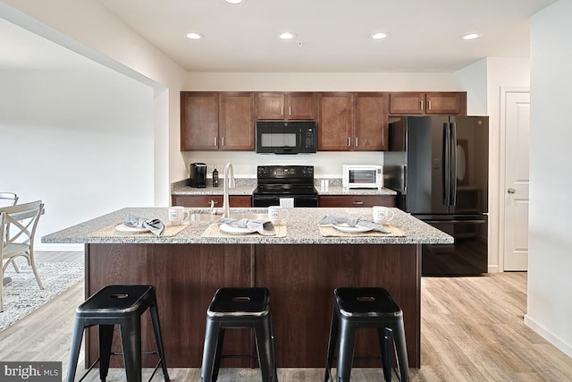 kitchen with an island with sink, sink, a kitchen bar, black appliances, and light hardwood / wood-style flooring