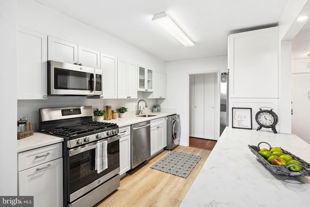 kitchen with white cabinetry, stainless steel appliances, light stone counters, and washer / dryer