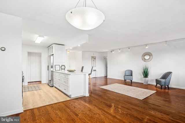 interior space featuring white cabinetry, hanging light fixtures, stainless steel refrigerator with ice dispenser, kitchen peninsula, and light wood-type flooring