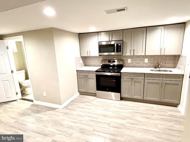 kitchen with decorative backsplash, gray cabinets, sink, and stainless steel appliances