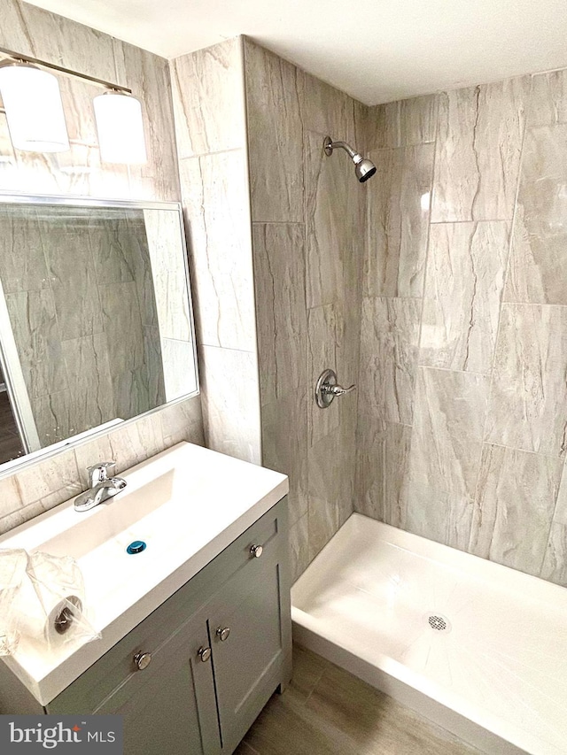 bathroom with a tile shower, vanity, and wood-type flooring