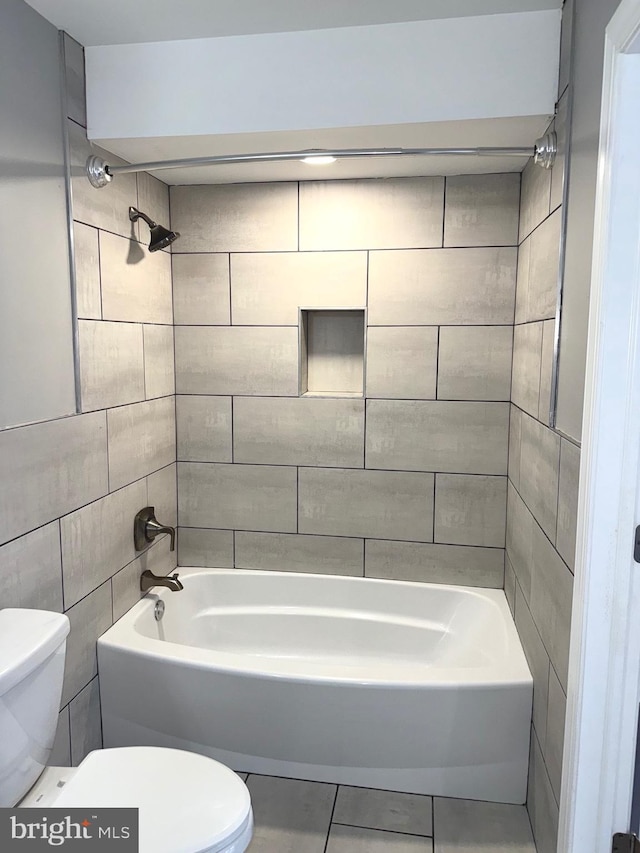 bathroom with toilet, tiled shower / bath combo, tile patterned flooring, and tile walls