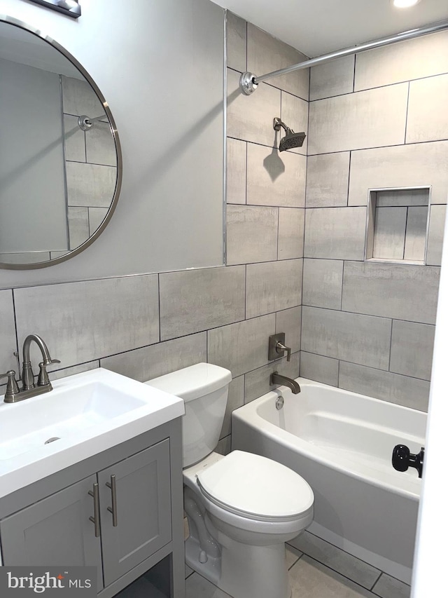 full bathroom featuring tiled shower / bath combo, vanity, tile walls, and toilet