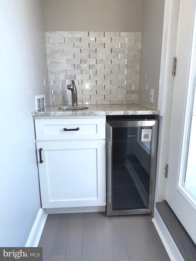 bar with sink, backsplash, light stone counters, white cabinets, and beverage cooler