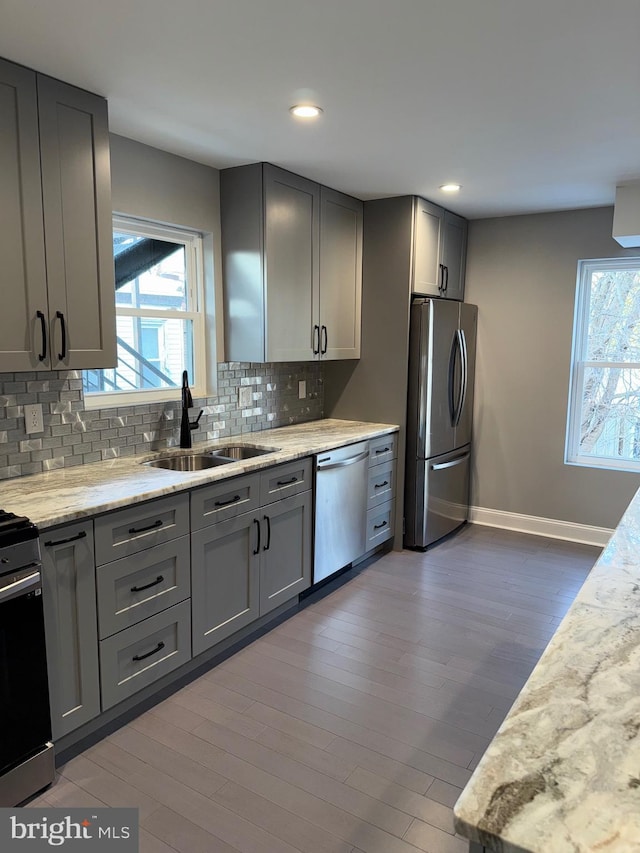 kitchen featuring sink, appliances with stainless steel finishes, gray cabinetry, backsplash, and light stone counters