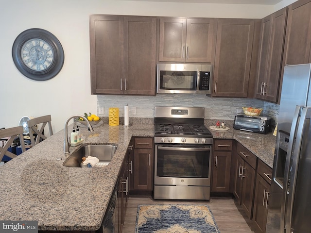 kitchen with sink, light stone countertops, light wood-type flooring, kitchen peninsula, and stainless steel appliances