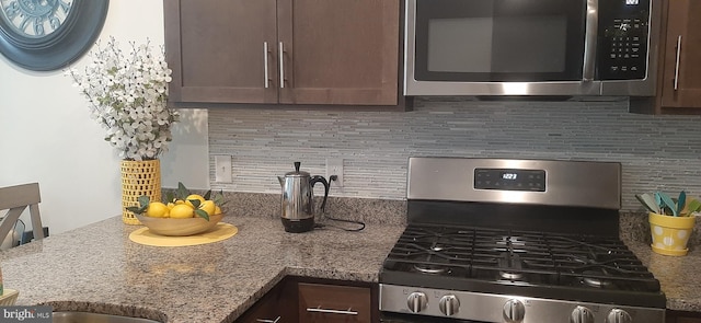 kitchen with decorative backsplash, dark brown cabinets, stainless steel appliances, and stone countertops