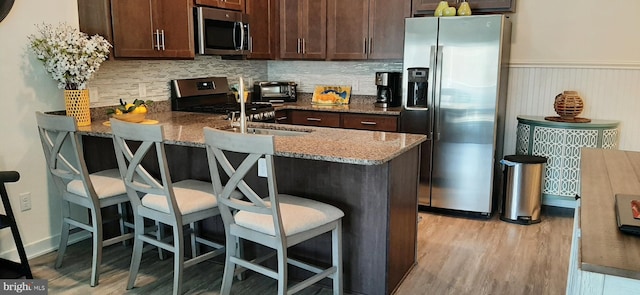 kitchen with dark brown cabinets, light stone counters, a breakfast bar area, and appliances with stainless steel finishes