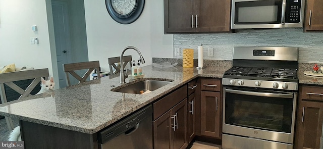 kitchen with light stone countertops, stainless steel appliances, kitchen peninsula, and sink