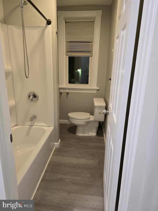 bathroom with washtub / shower combination, hardwood / wood-style flooring, and toilet