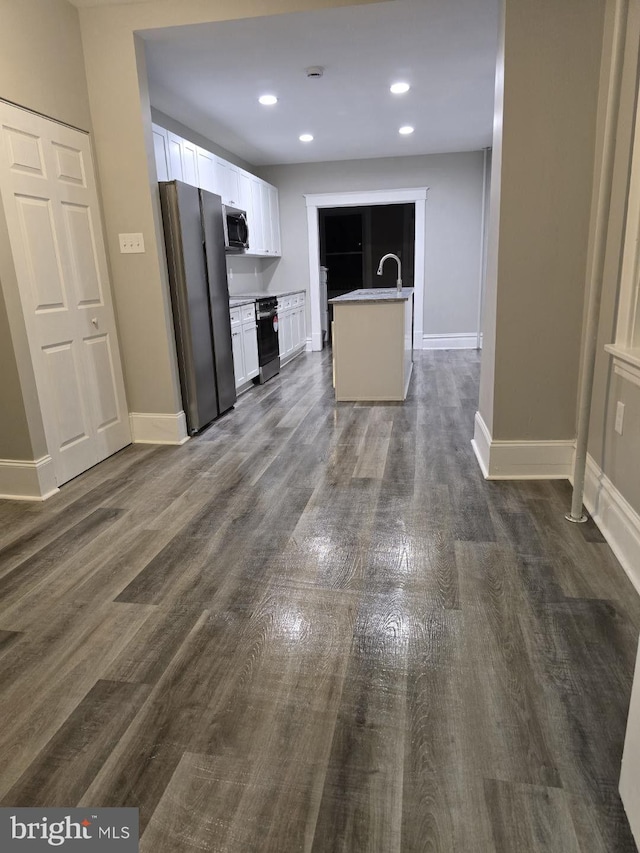 kitchen featuring dark hardwood / wood-style flooring, a center island with sink, white cabinetry, and stainless steel refrigerator