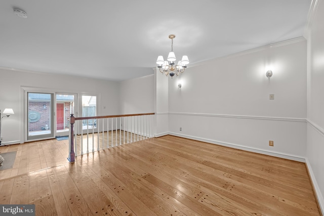 spare room with an inviting chandelier, crown molding, and light hardwood / wood-style flooring