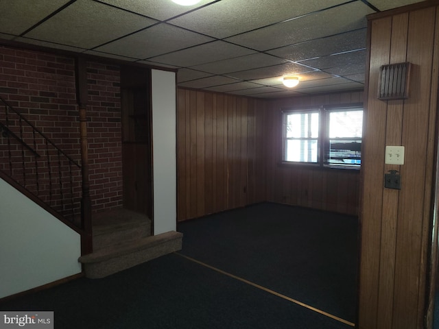 basement with a drop ceiling and wooden walls