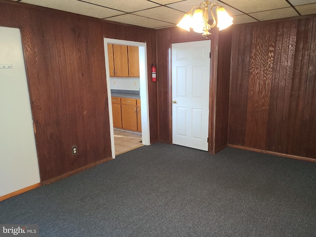 carpeted empty room with an inviting chandelier and wooden walls