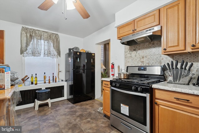 kitchen featuring light stone countertops, black fridge, stainless steel gas stove, backsplash, and ceiling fan