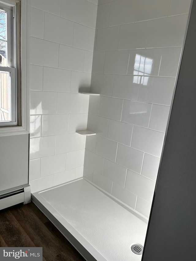 bathroom with a tile shower, hardwood / wood-style floors, a baseboard radiator, and a healthy amount of sunlight