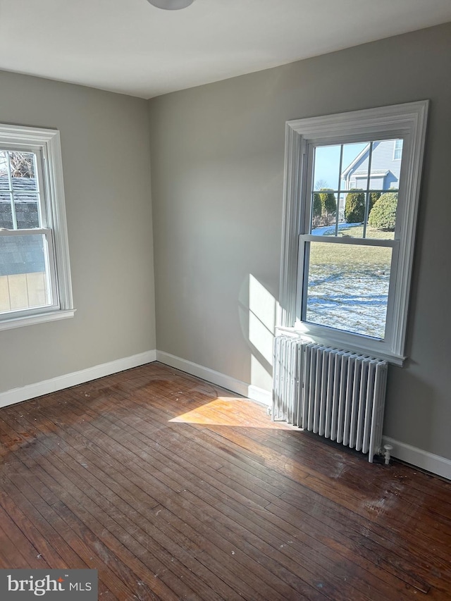 empty room with dark hardwood / wood-style flooring, radiator, and a wealth of natural light