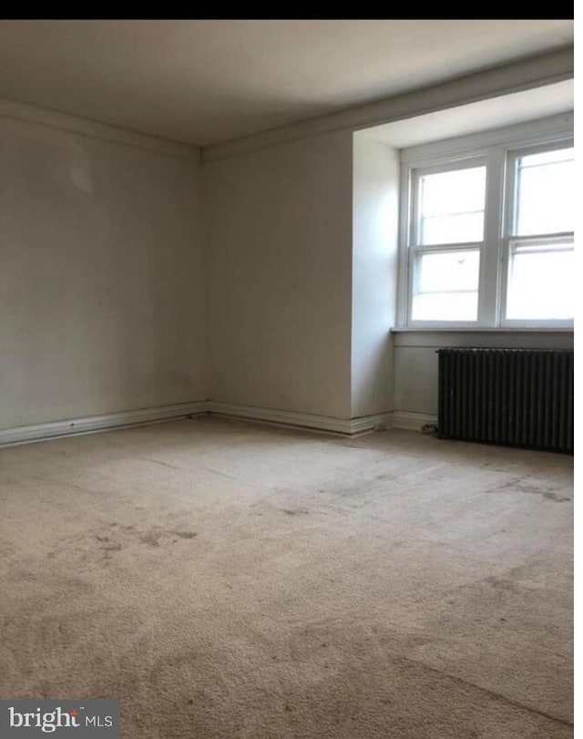 empty room featuring ornamental molding, light carpet, and radiator