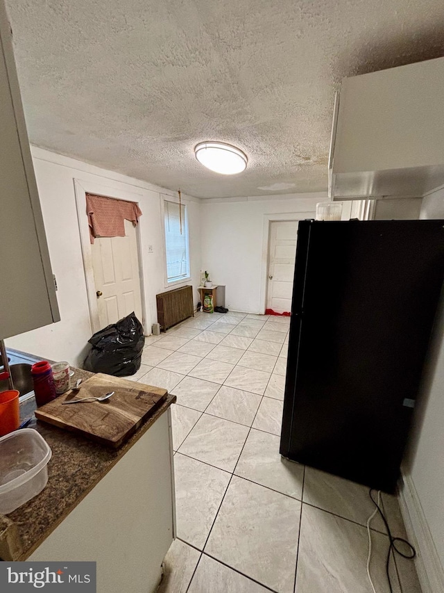 kitchen featuring a textured ceiling, black fridge, radiator, and light tile patterned flooring