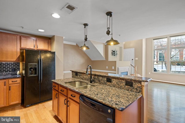 kitchen with dishwasher, sink, hanging light fixtures, black fridge, and an island with sink