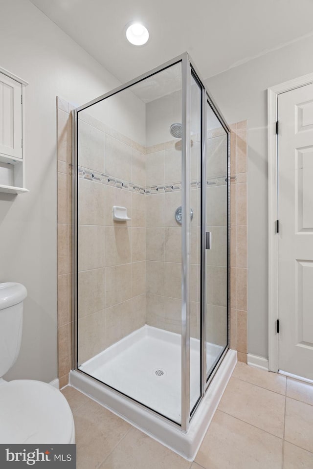 bathroom with tile patterned flooring, toilet, and a shower with door