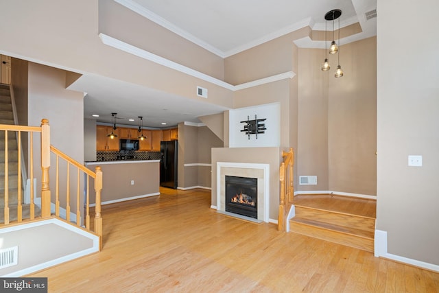 unfurnished living room featuring crown molding, light hardwood / wood-style flooring, and a high ceiling