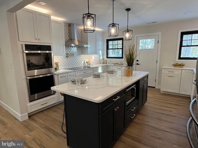 kitchen with hanging light fixtures, double oven, a kitchen island, wall chimney exhaust hood, and white cabinetry