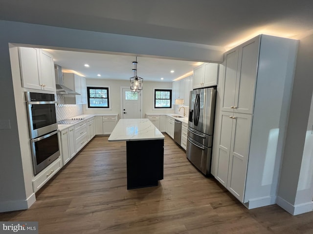 kitchen featuring wall chimney exhaust hood, pendant lighting, a center island, white cabinets, and appliances with stainless steel finishes