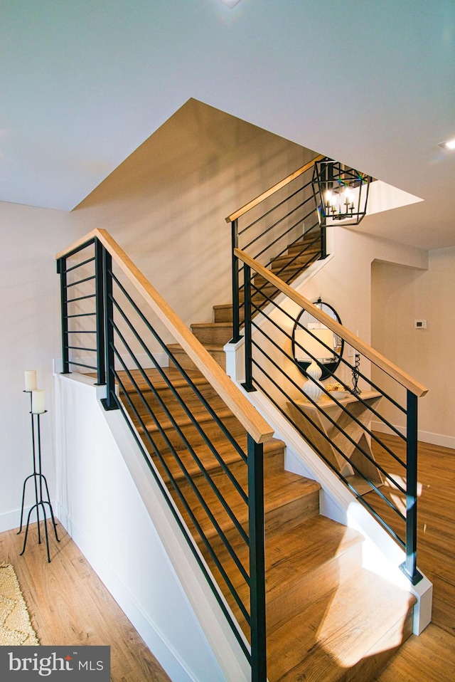 stairway with hardwood / wood-style floors and a chandelier