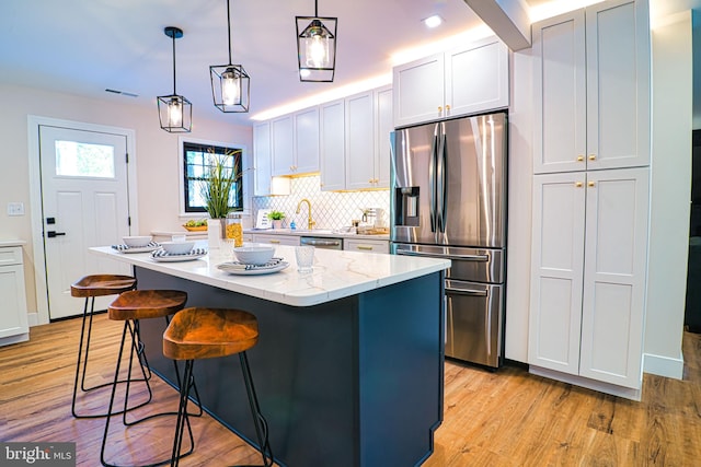 kitchen with stainless steel appliances, light stone counters, light hardwood / wood-style flooring, hanging light fixtures, and a kitchen island