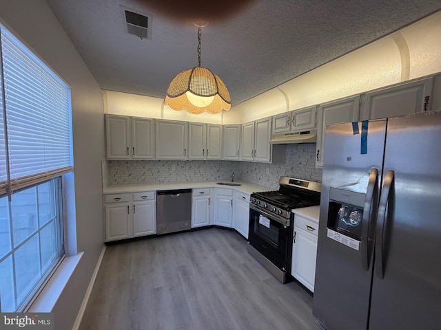 kitchen featuring sink, stainless steel appliances, light hardwood / wood-style floors, pendant lighting, and a textured ceiling